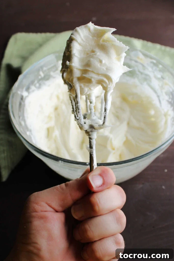 Velvety Cream Cheese Frosting 3 Mixer beater filled with cream cheese frosting.