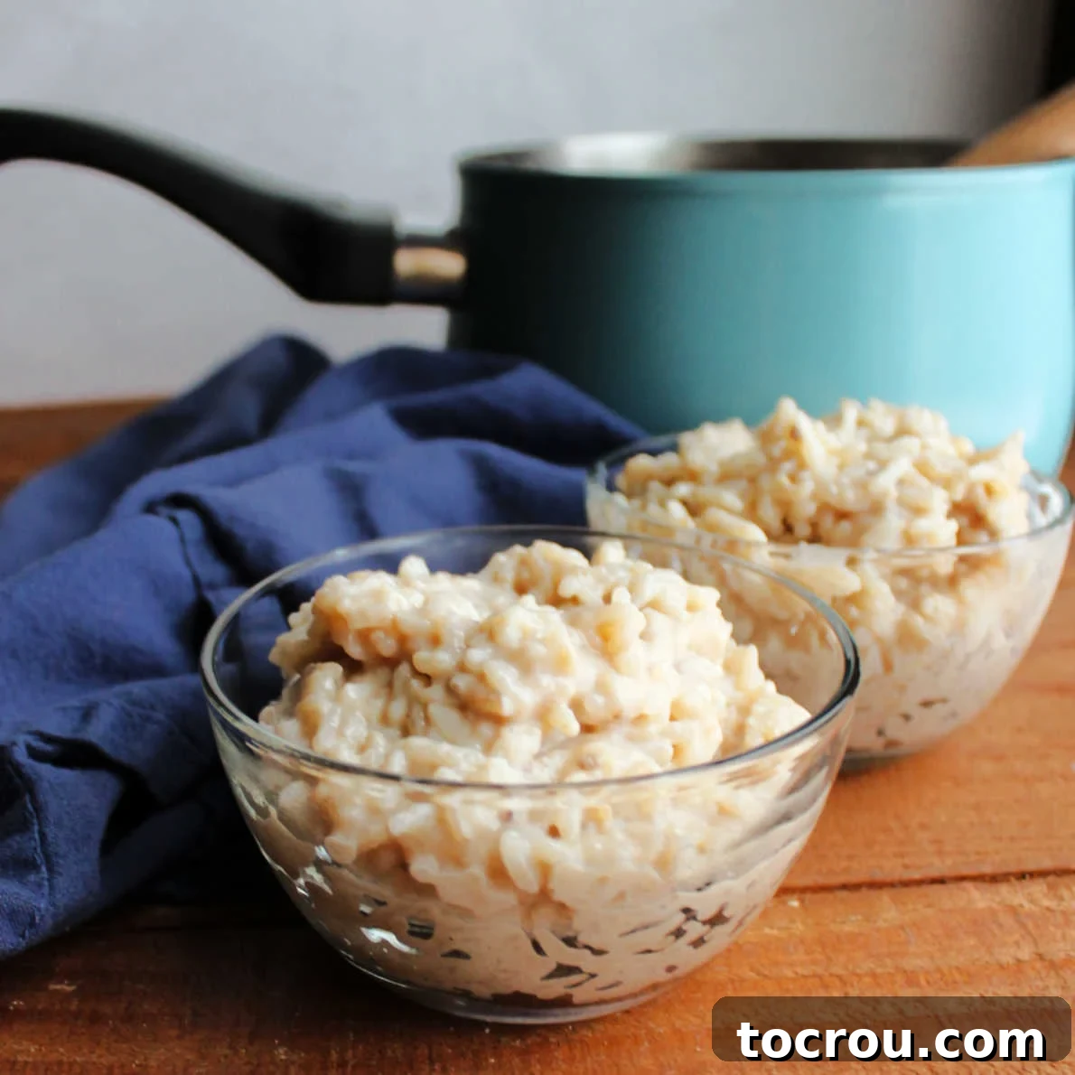 Bananas, rice, milk and honey team up in this delicious treat. These wholesome ingredients let you feel good about it too! Two small glass bowls of creamy rice pudding sweetened with banana and honey in front of blue saucepan.