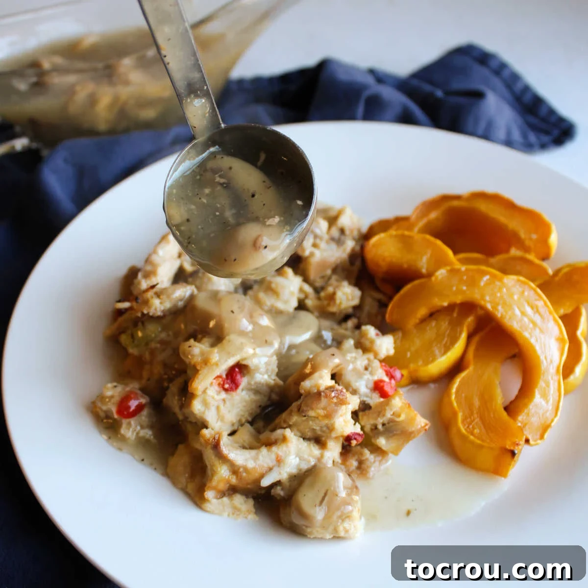 This turkey casserole feeds a crowd. It was served at MiMi's bridal shower and she still talks about it. We really enjoy it too! Spooning rich mushroom gravy over a serving of golden-brown turkey and rice casserole, garnished with roasted squash on a rustic plate.