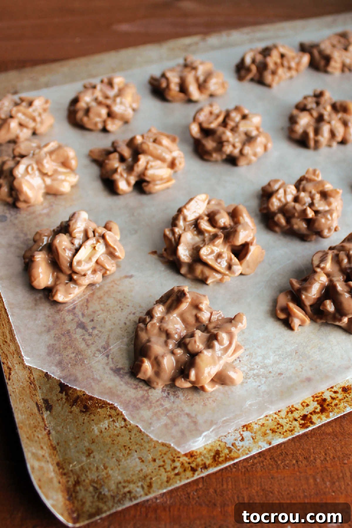 Effortless Crockpot Peanut Delights 6 Scoops of peanut cluster mixture on wax paper setting up.