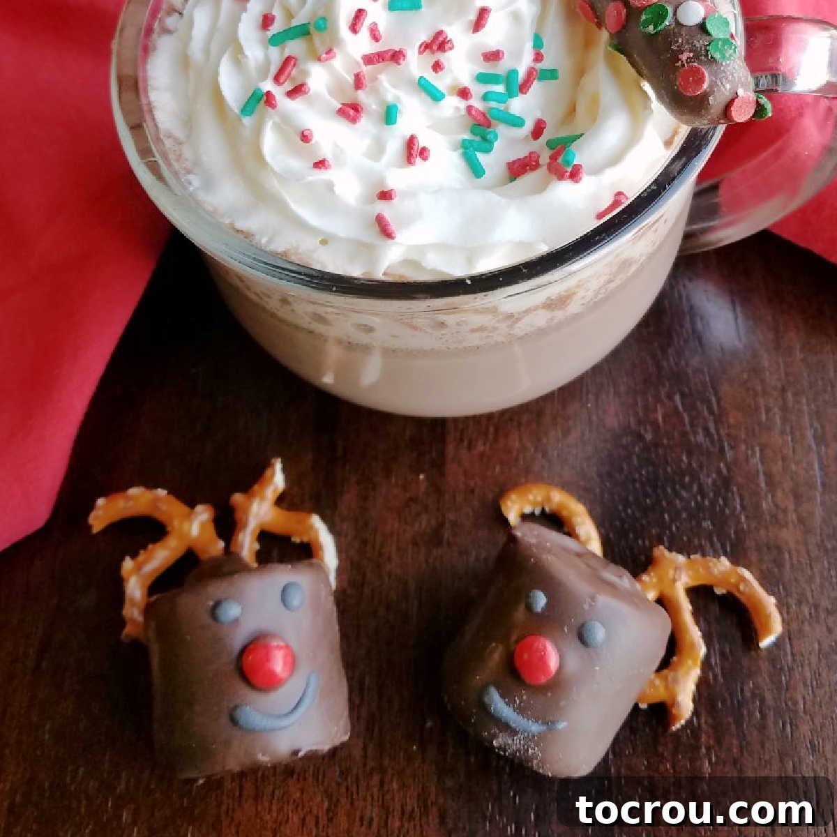 These Rudolph the marshmallow reindeer are so cute and the perfect accompaniment to your mug of hot cocoa! Chocolate dipped marshmallows decorated to look like rudolph next to mug of hot chocolate topped with whipped cream and sprinkles.
