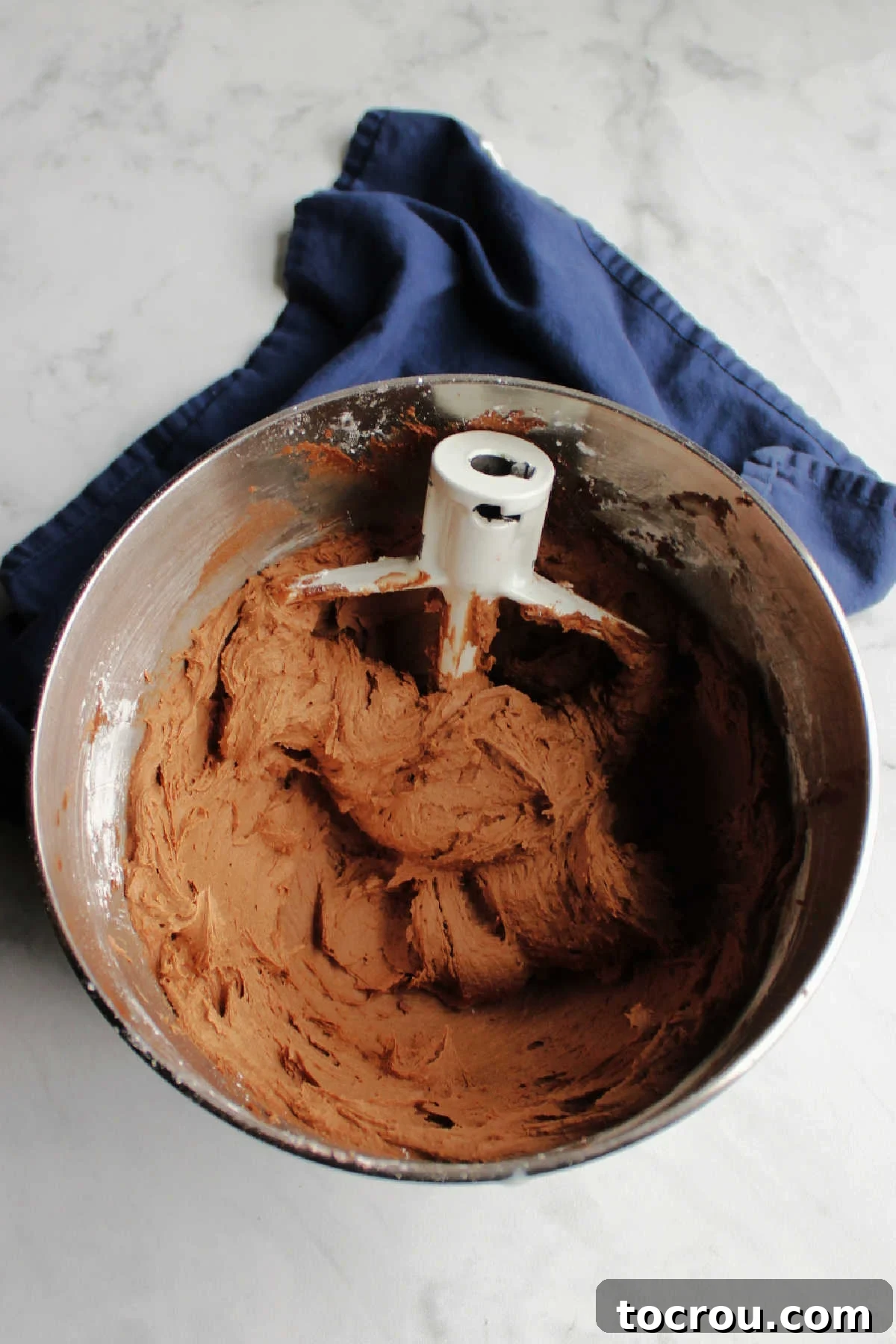 Mixer bowl filled with brownie batter frosting and a mixer paddle.