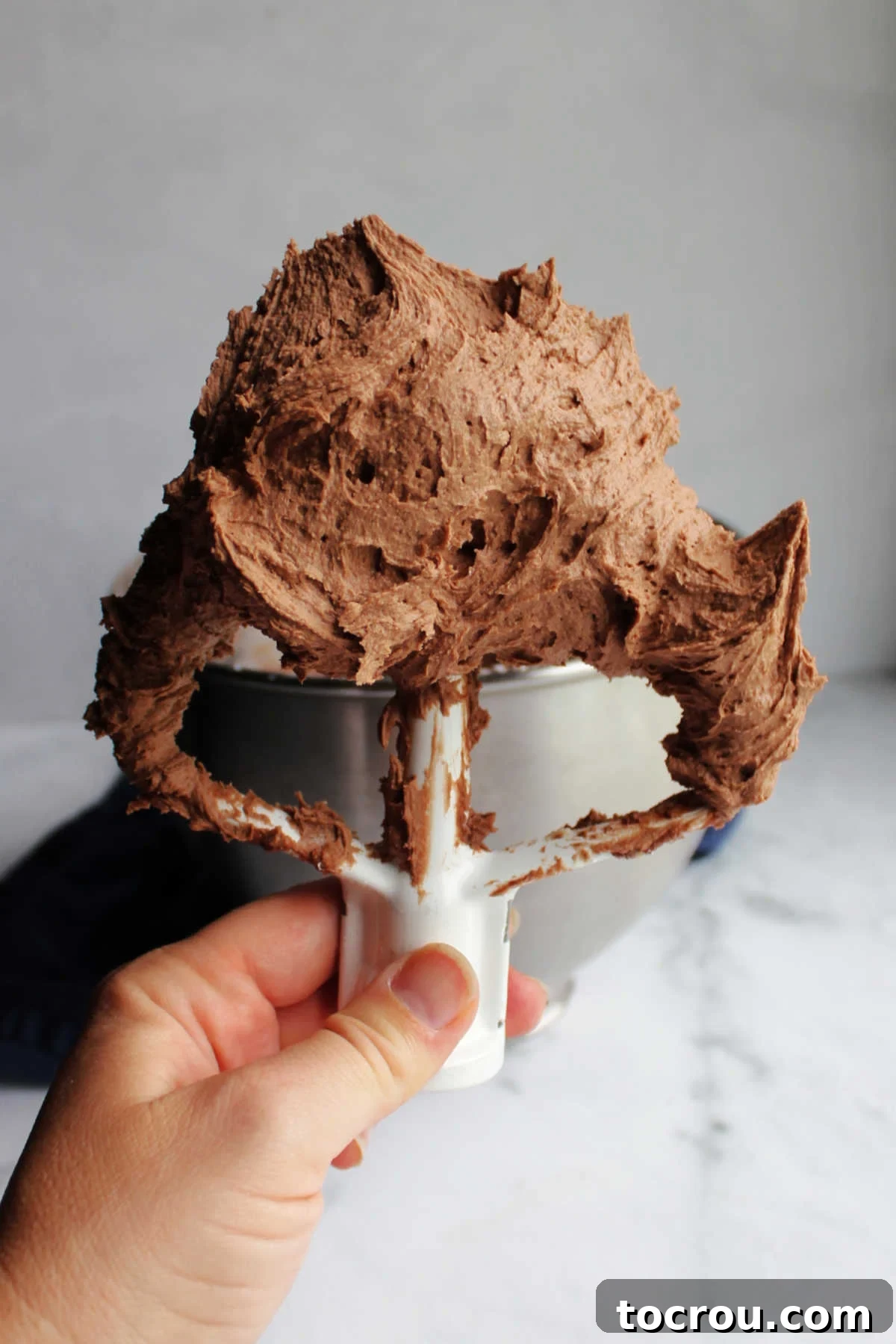 Hand holding mixer paddle with lots of brownie batter frosting on it.