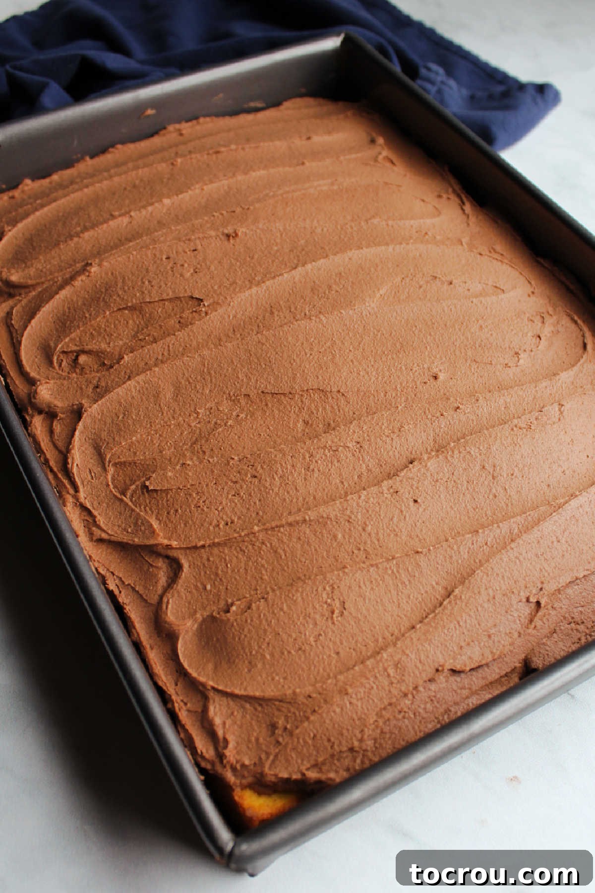 chocolate brownie batter frosting spread over 9x13 inch cake with swirls left behind by spatula.