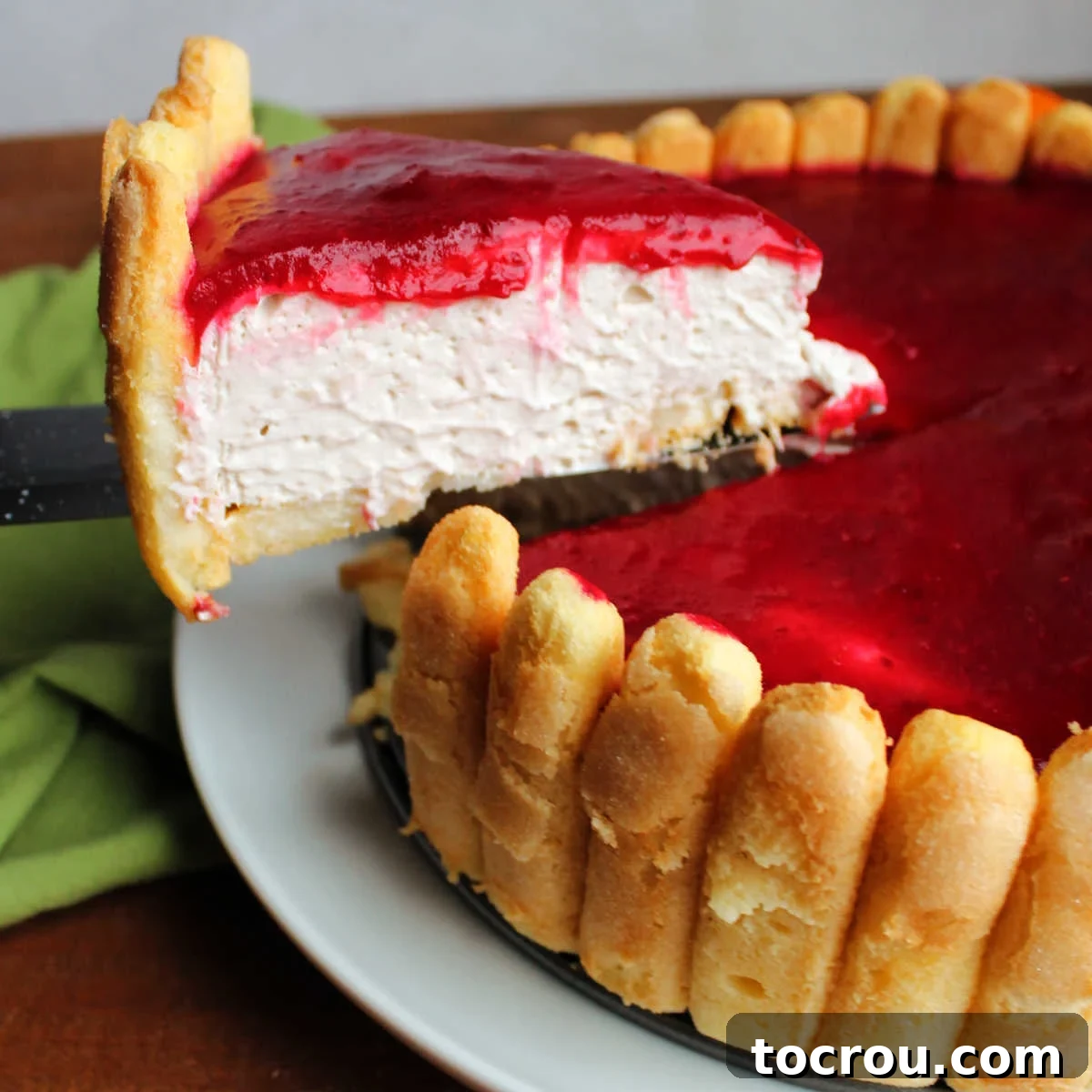 Lifting first slice of Charlotte Russe up, showing smooth mousse like orange banana filling, lady finger crust and cranberry sauce topping.