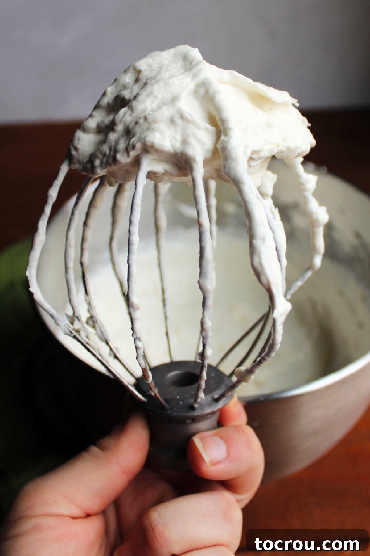 Fluffy creamy orange and banana filling on a balloon whisk showing stiff peaks. 