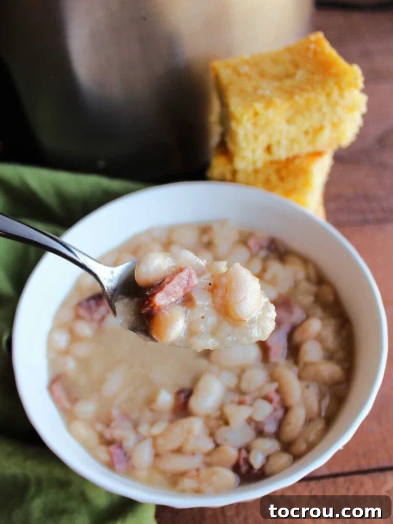 Spoonful of Ham and Beans A spoonful of rich ham and beans, with cornbread in the background and a slow cooker, ready for a warm and hearty meal.