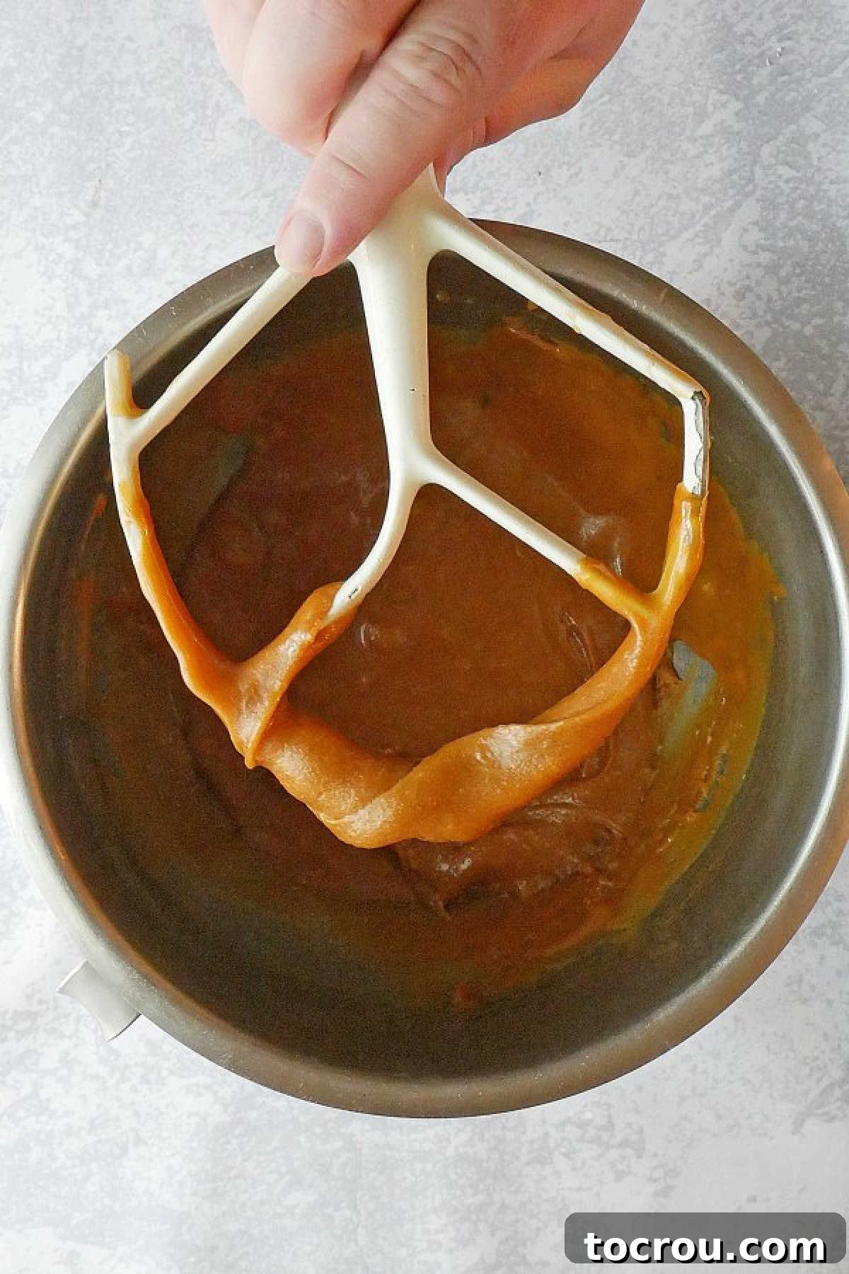 Southern Gold Caramel Frosting 5 Hand holding mixer paddle with caramel frosting on it.