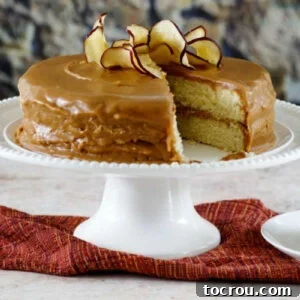 Southern caramel cake with homemade caramel icing topped with apple chips on a white cake pedestal.
