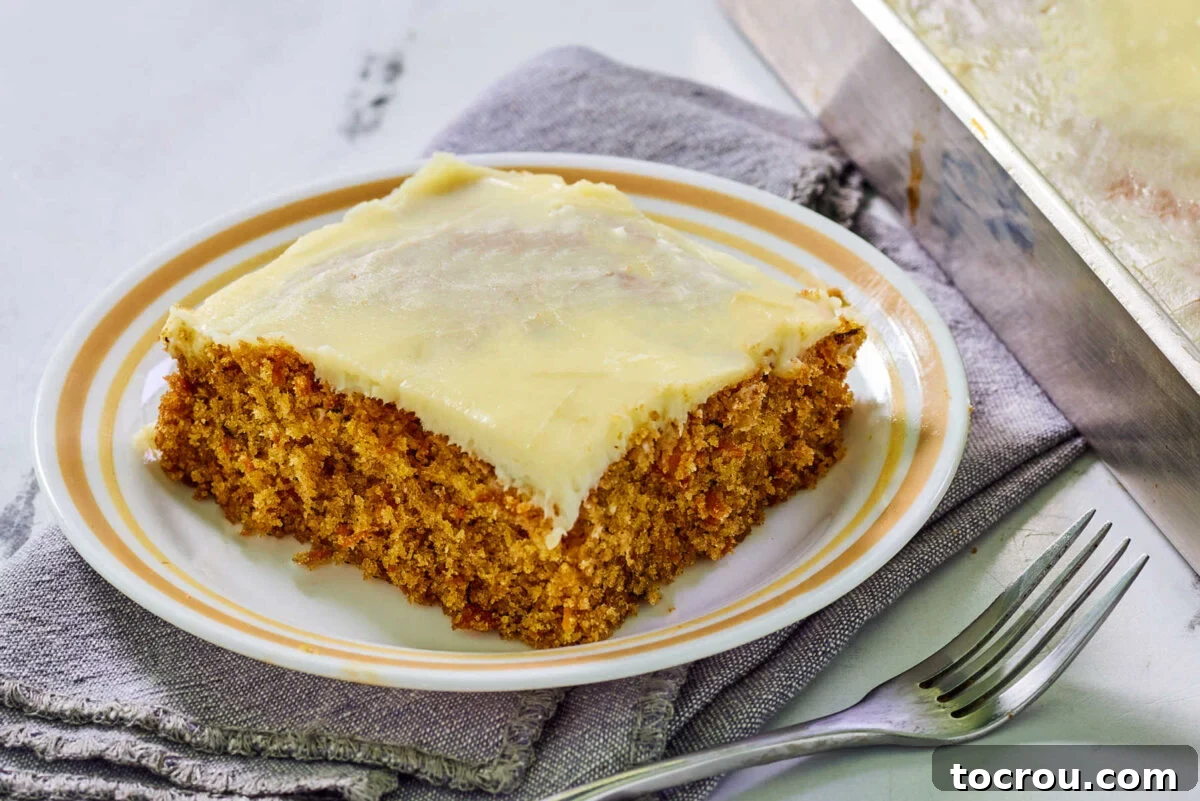 Dessert plate with a slice of homemade carrot cake topped with cream cheese frosting next to a fork, ready to eat.