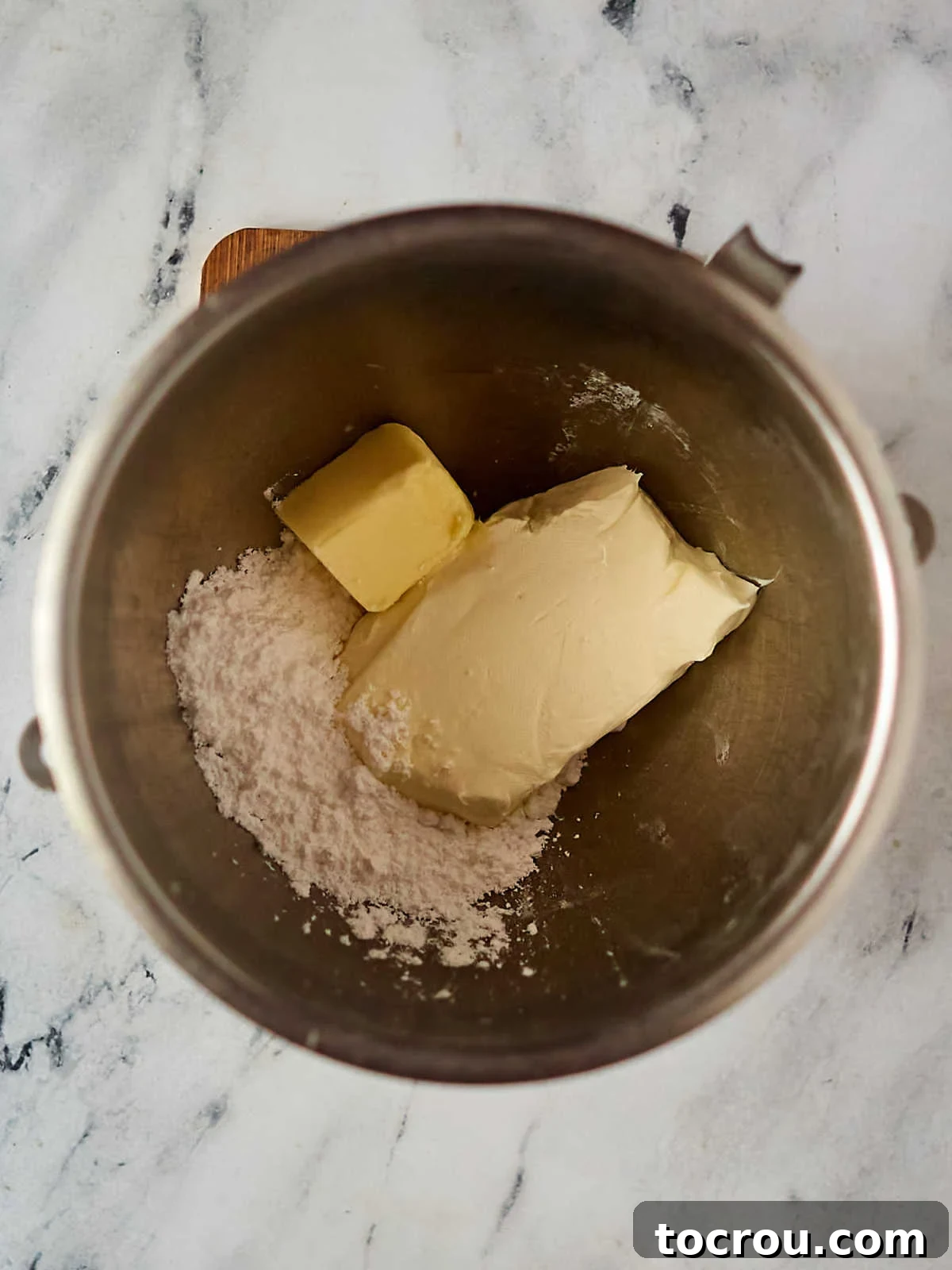 Mixer bowl with powdered sugar, butter and cream cheese inside, ready to make frosting.