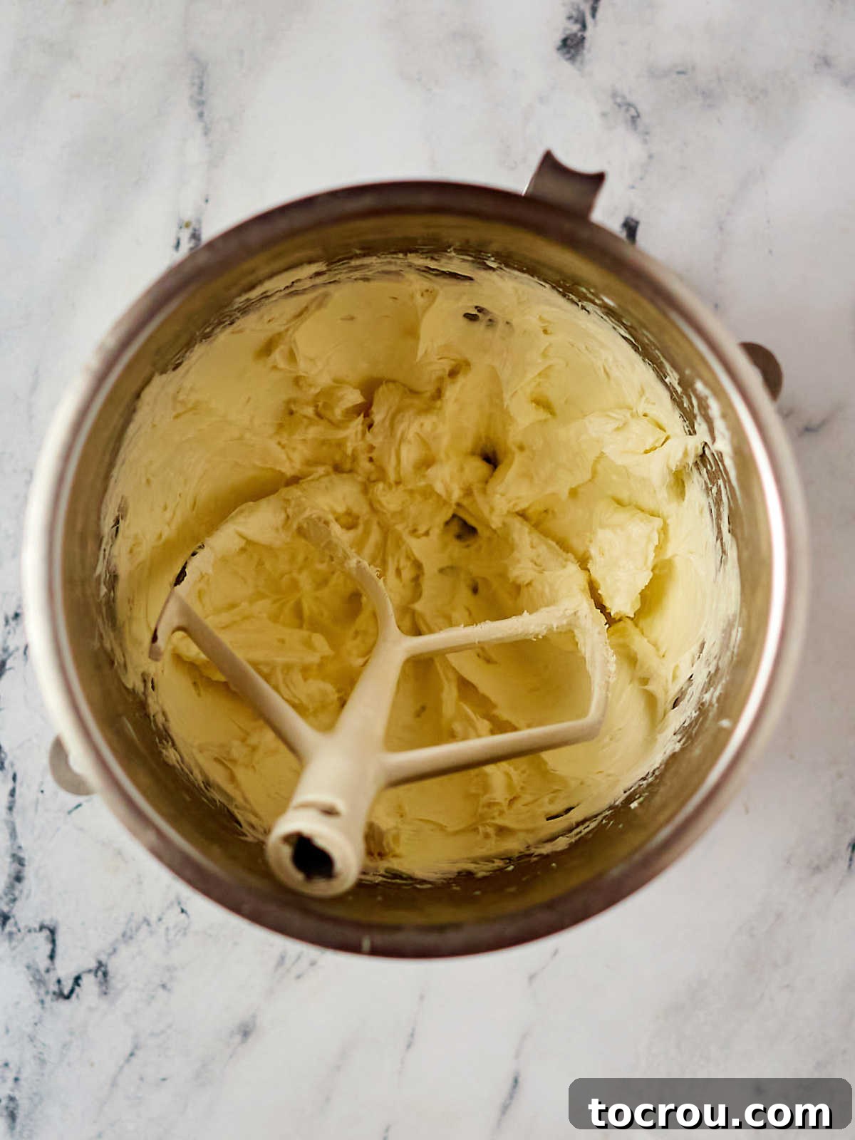 Mixer bowl with smooth cream cheese frosting inside with a paddle attachment, ready to use.