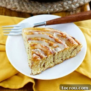 Big slice of pumpkin spice cinnamon roll cake drizzled with maple browned butter glaze on plate with fork.