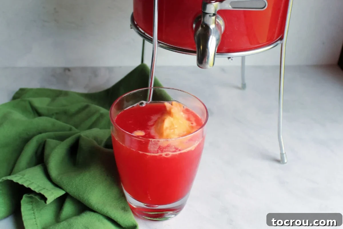 Glass of pink aloha punch with orange sherbet floating on top, ready to drink.