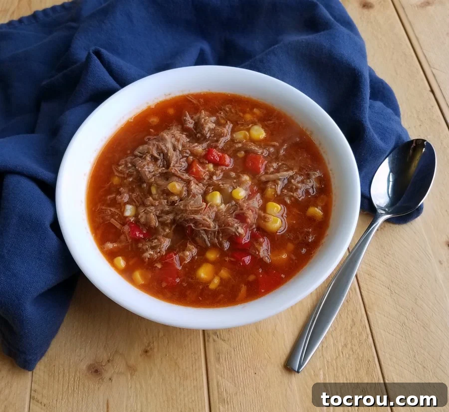 Delicious Brunswick Stew with Smoked Meats A steaming bowl of Brunswick stew, showcasing tender pieces of leftover BBQ meat, sweet corn, and diced tomatoes, served with a spoon.