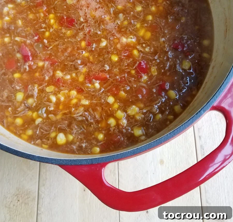 Brunswick Stew in a Dutch Oven An enameled cast iron Dutch oven filled with a rich, tomato-based Brunswick stew, featuring visible chunks of pulled pork, chicken, brisket, and corn.