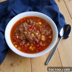 Bowl of brunswick stew with leftover bbq meat, corn and tomatoes in bowl with spoon.