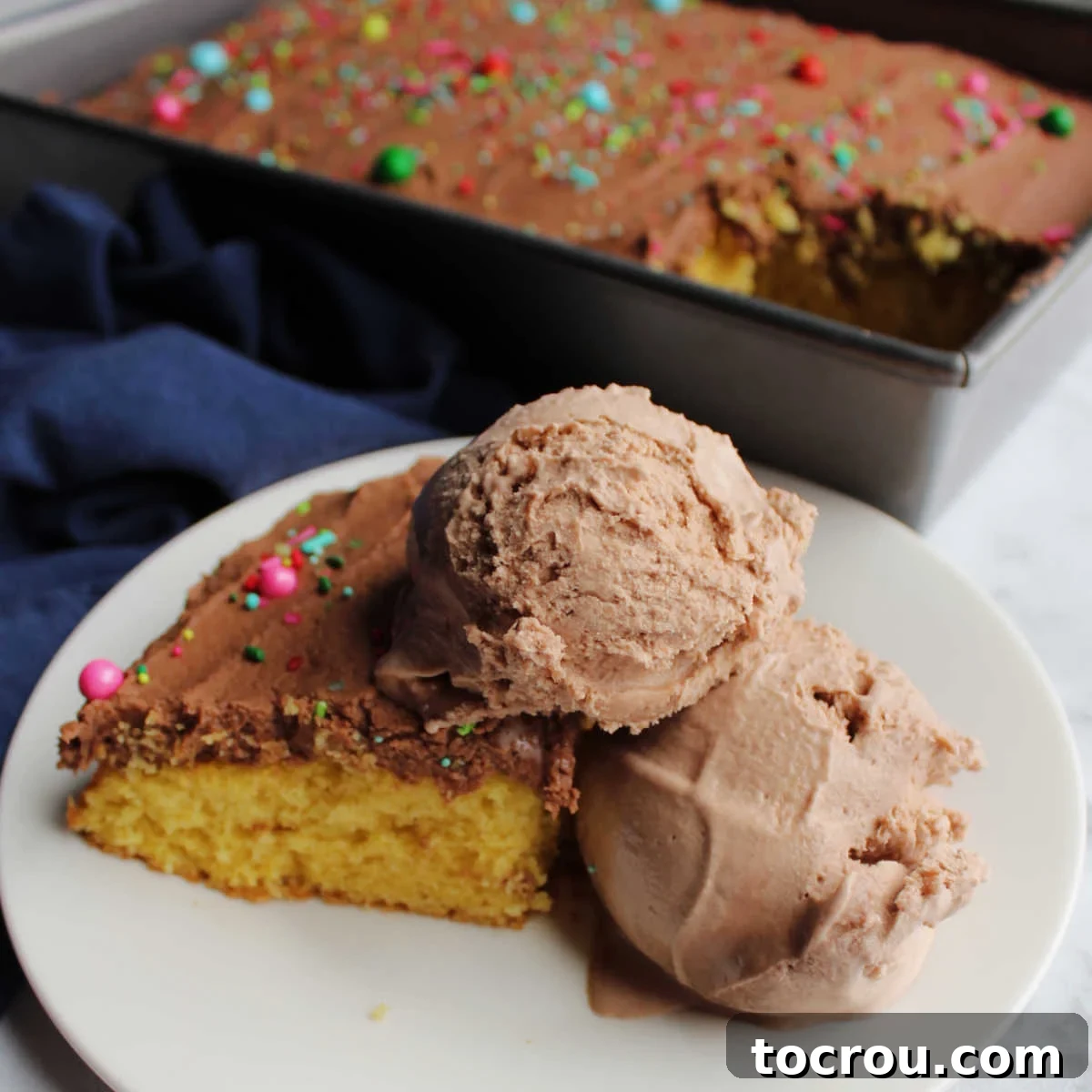 Close piece of cake with chocolate frosting and scoops of brownie batter ice cream ready to eat.