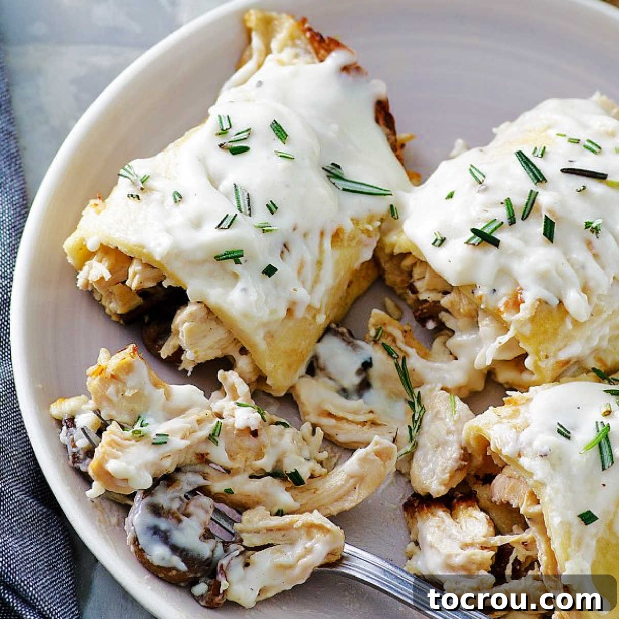 Forkful of creamy lemon bechamel covered chicken and mushroom stuffed crepes, showing the rich texture of the sauce.