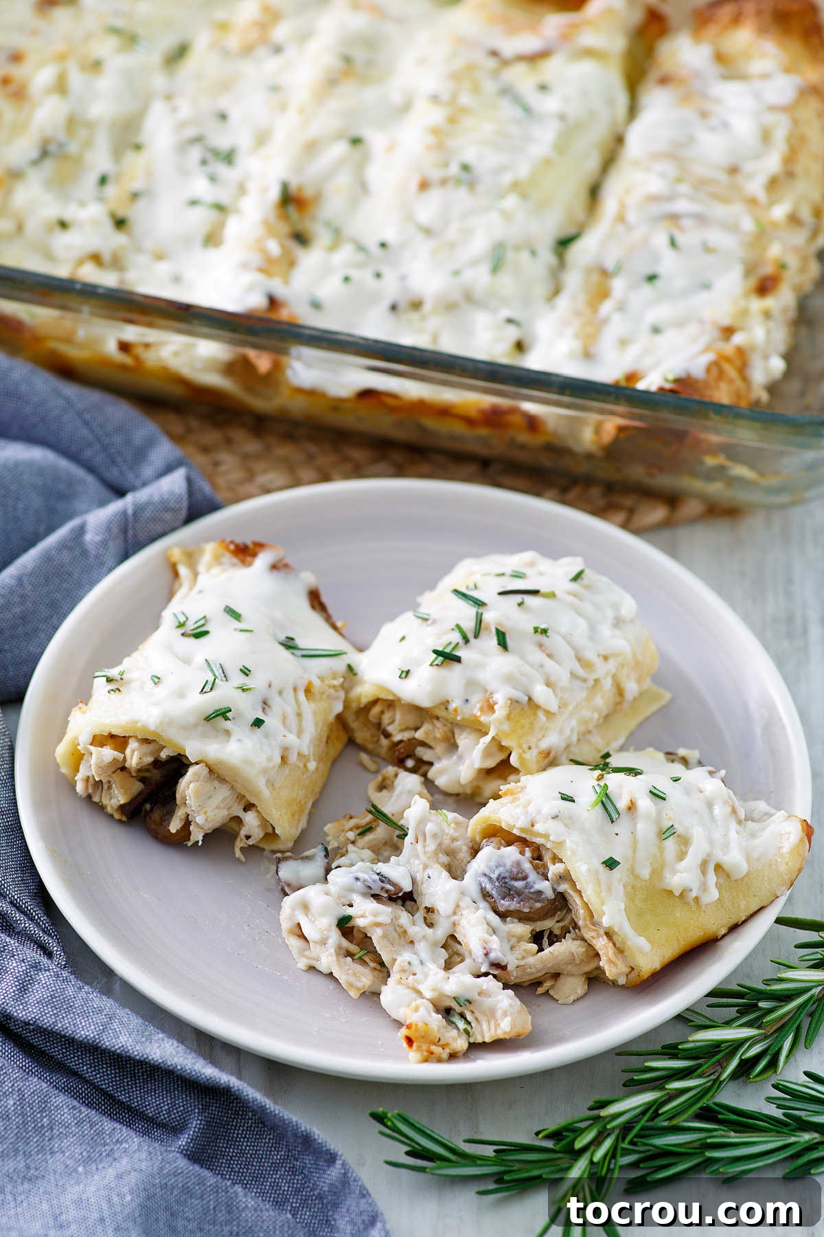 Creamy chicken and mushroom crepes with lemon rosemary bechamel served on a plate, with a pan of crepes visible in the background.