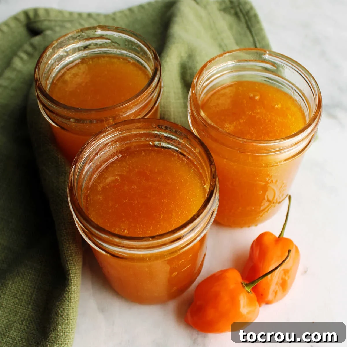 Jars of freshly made habanero peach jelly with orange habaneros nearby.
