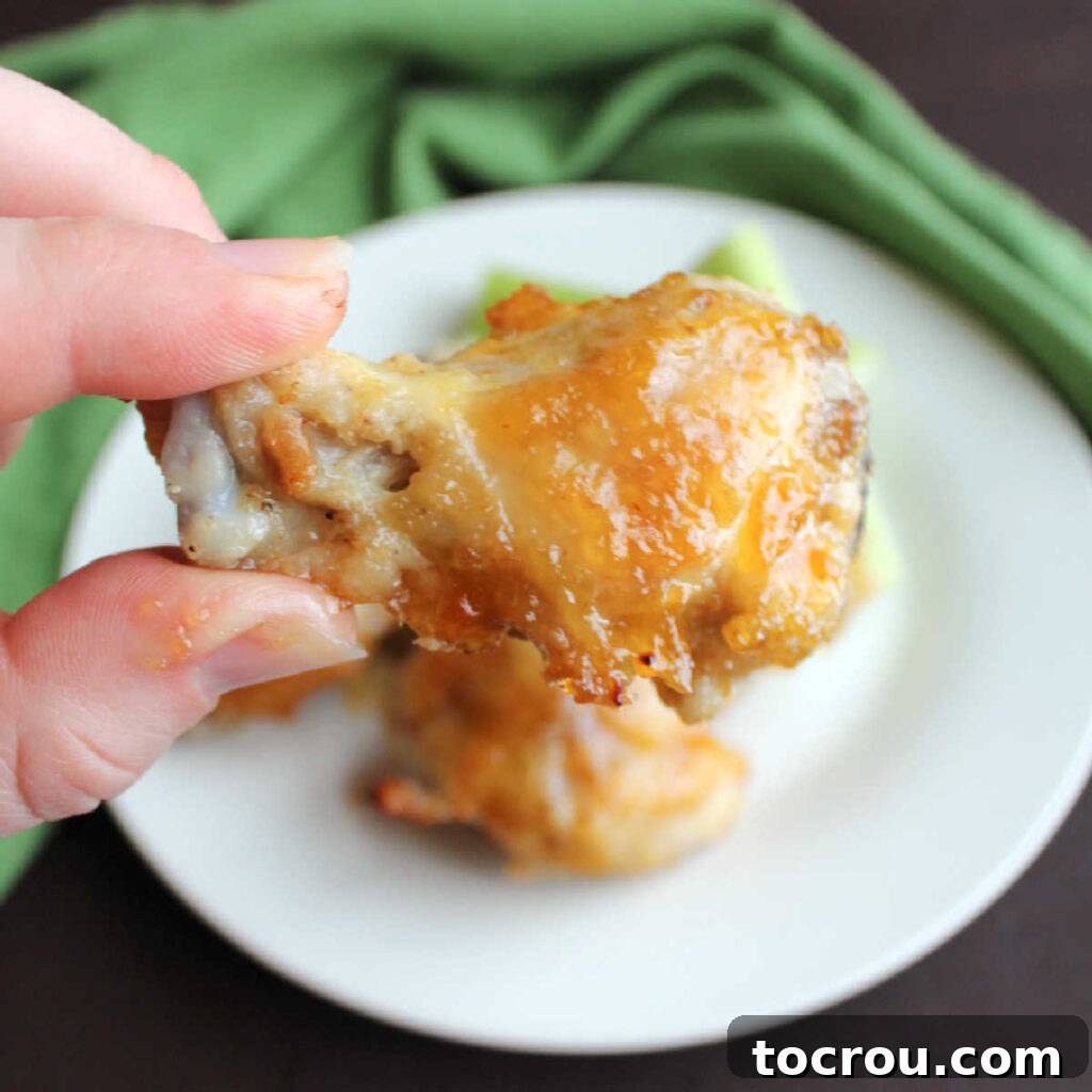 Hand holding wing drummie coated in peach habanero sauce.