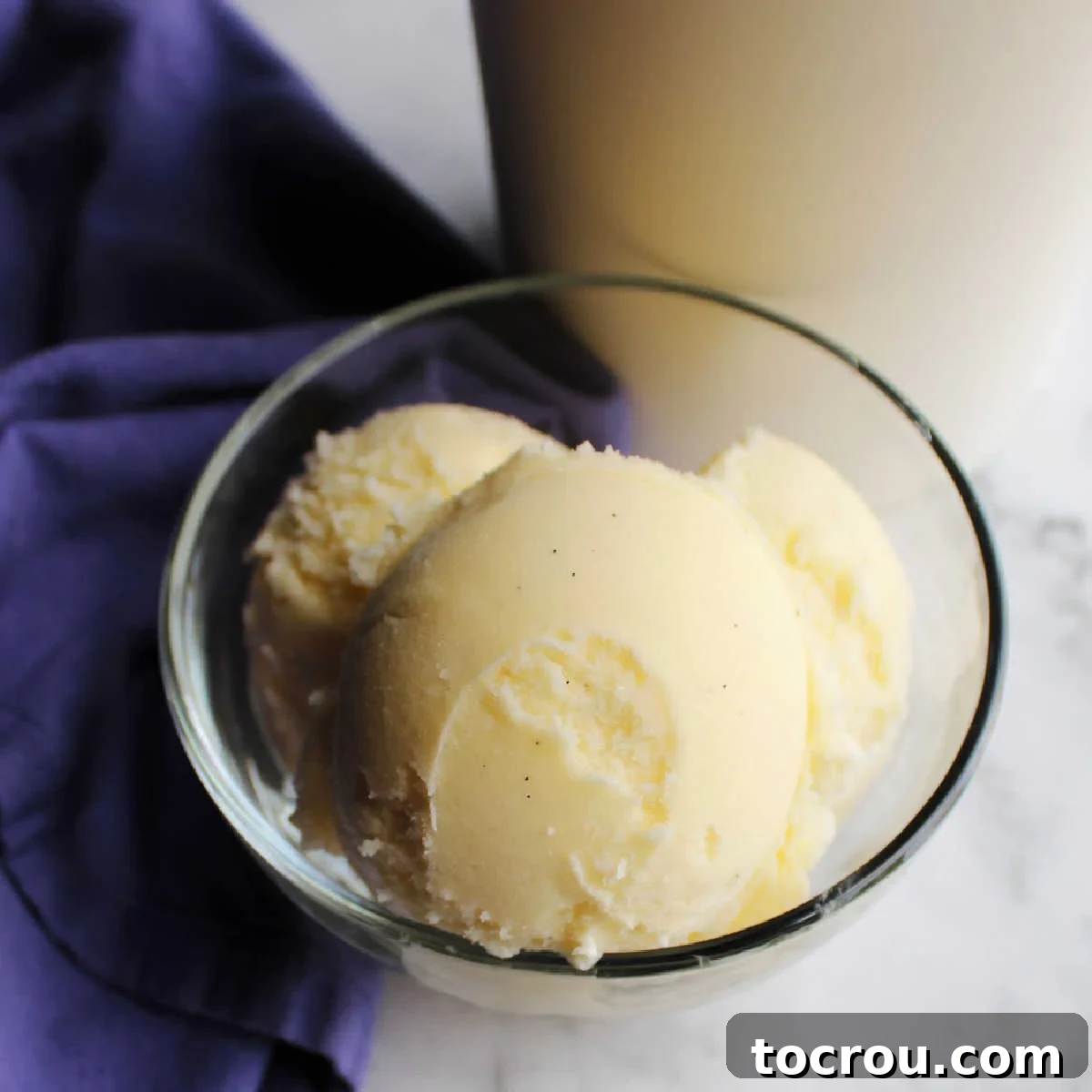 Scoops of smooth creamy vanilla ice cream in glass bowl by storage container.