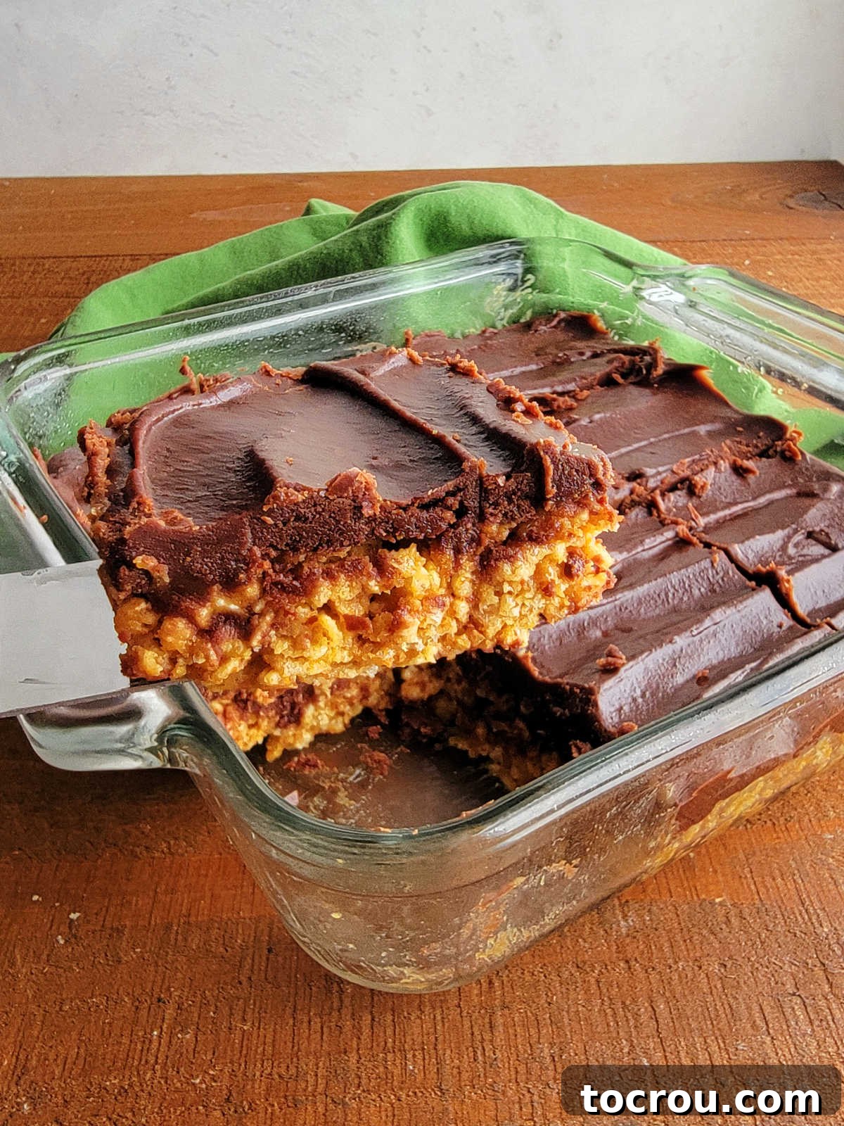 Spatula lifting a piece of maple peanut butter rice krispie treat, perfectly coated with a generous layer of homemade chocolate fudge icing, out of a baking pan.