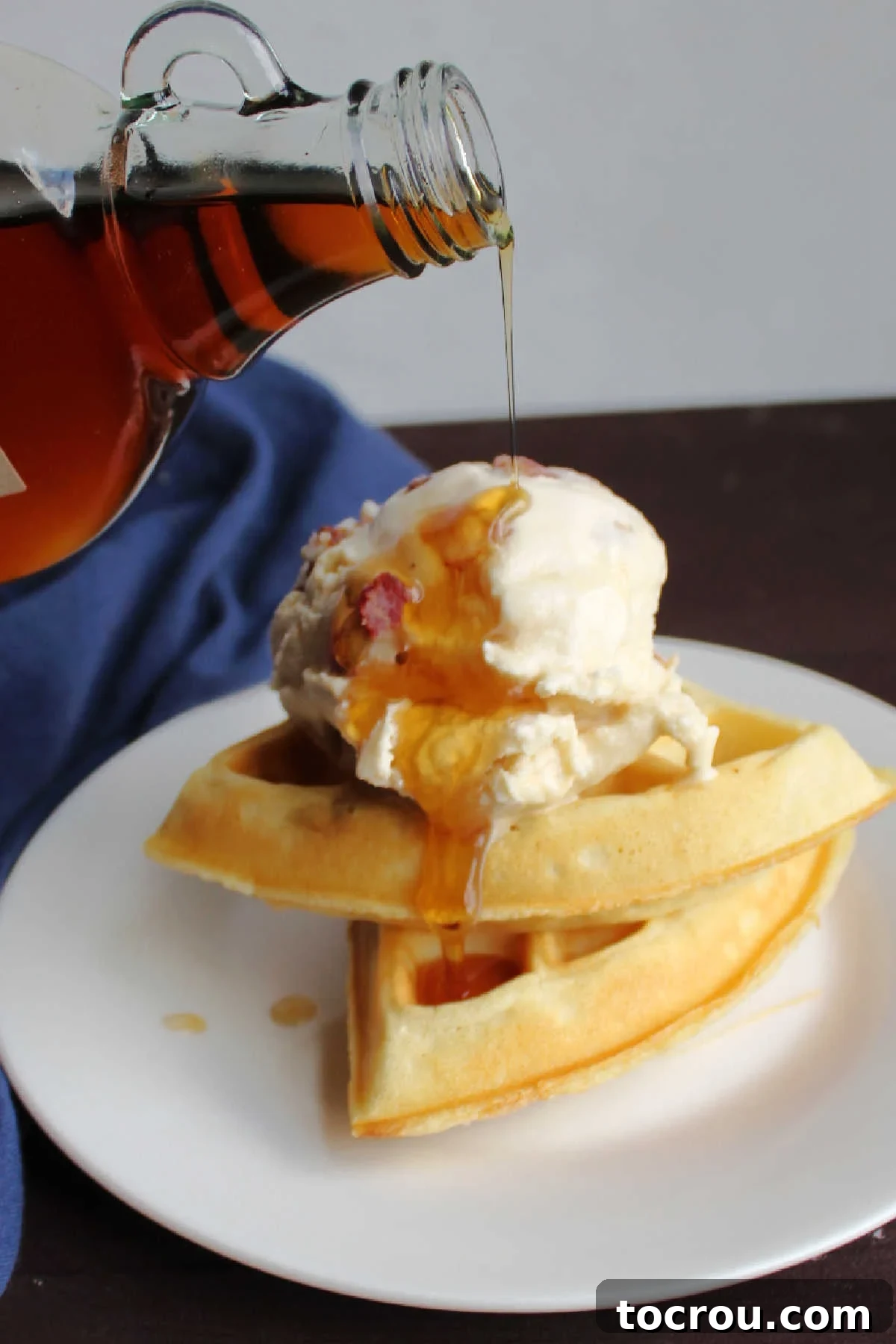 Maple Bacon Bliss Ice Cream 7 Pouring maple syrup over scoop of maple bacon ice cream perched on top of a couple pieces of Belgian waffle.