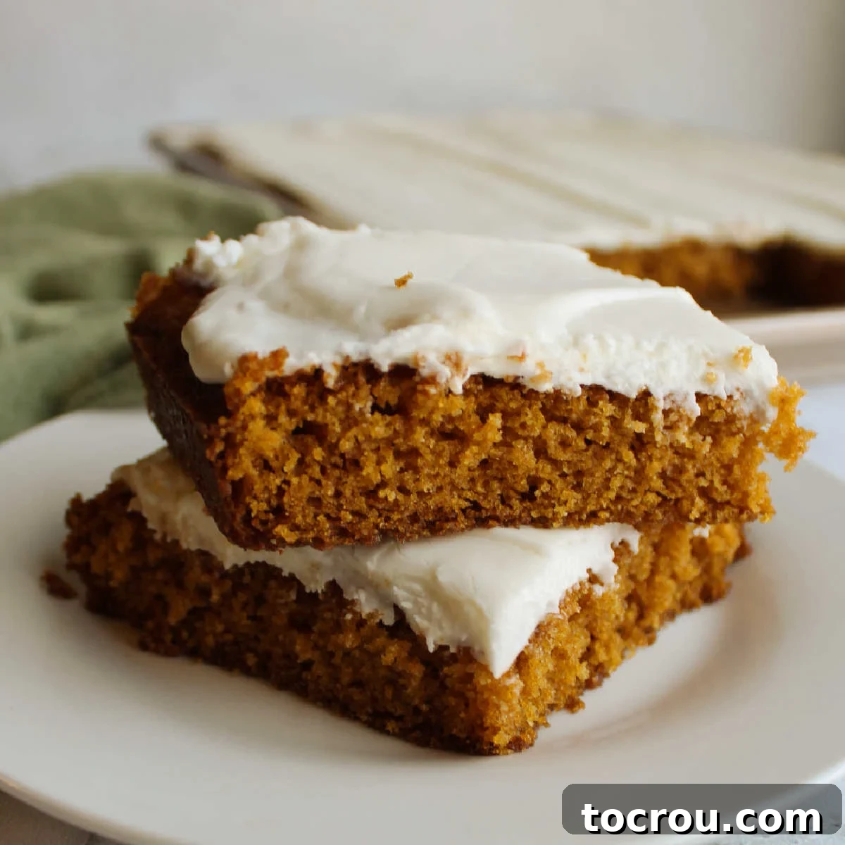 Stack of moist pumpkin bars topped with a generous swirl of tangy cream cheese frosting.