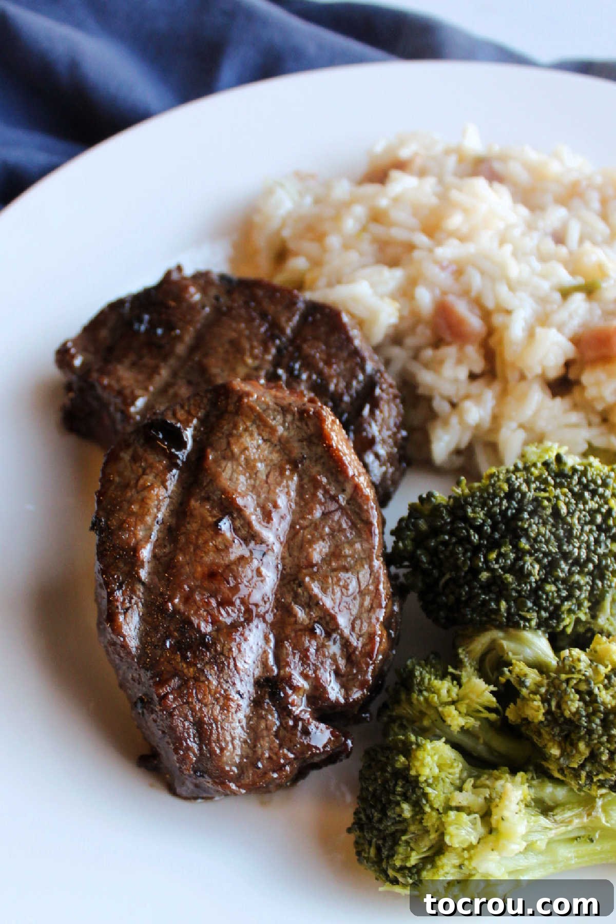 A mouth-watering dish of grilled venison backstrap, perfectly marinated in Bulgogi sauce, served with fresh broccoli and rice. Grilled venison backstrap with bul kogi marinade on plate with broccoli and rice.