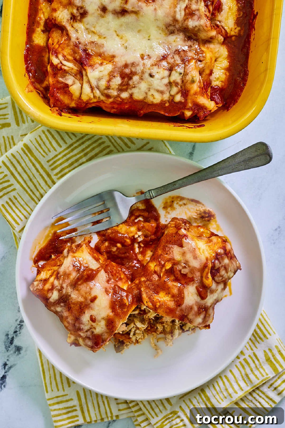 Chicken Enchilada with Red Sauce A plate featuring a chicken enchilada generously coated in homemade red sauce and topped with melted cheese, with a fork poised to take a bite.