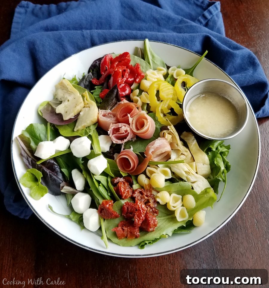 Green salad topped with veggies, cheese, pasta, meat and a container of homemade Parmesan salad dressing.