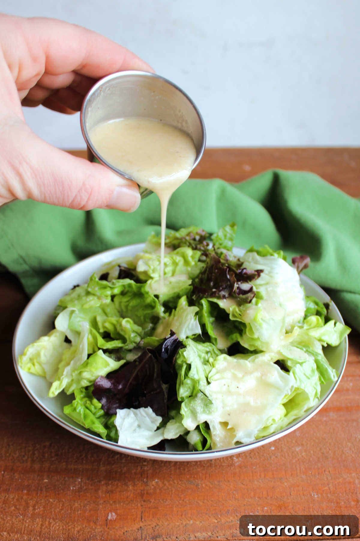 Pouring homemade salad dressing with parmesan cheese, herbs, and garlic over a bowl of lettuce.