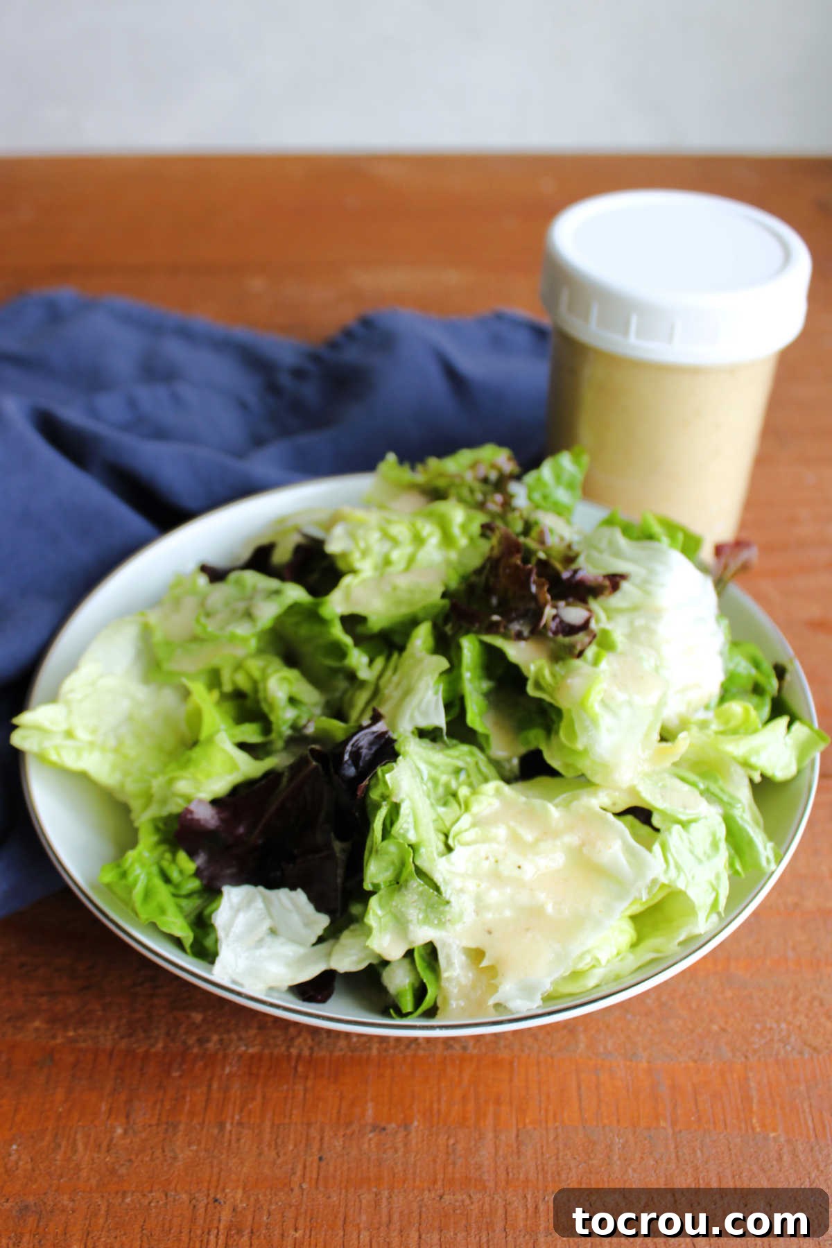 Lettuce dressed with homemade parmesan salad dressing next to a jar with more salad dressing inside. 