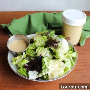 Bowl of lettuce with a ramekin of homemade salad dressing that looks creamy from the addition of Parmesan cheese next to a jar with more salad dressing inside.