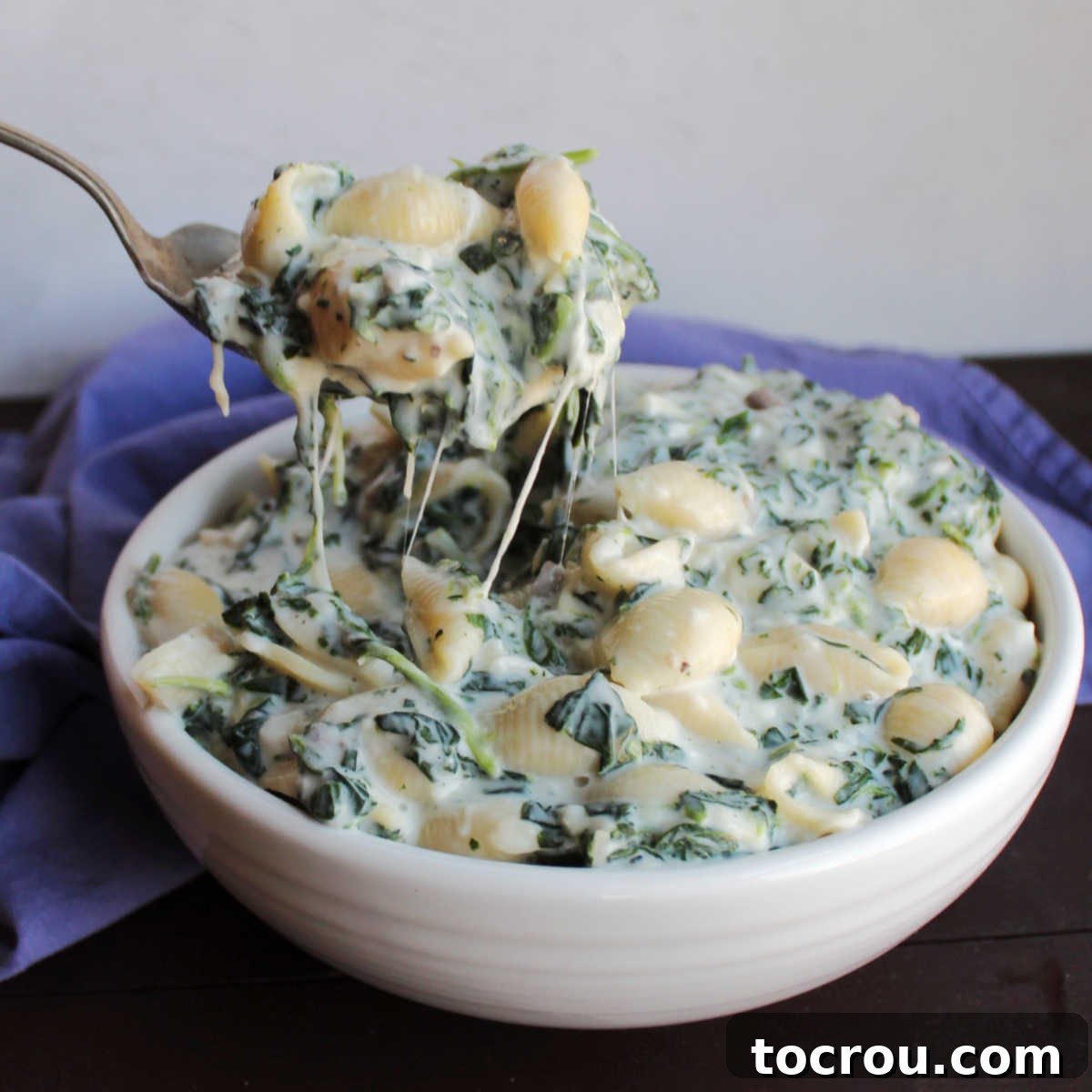 Velvety Spinach Macaroni Bake 2 Serving spoon filled with creamy white mac and cheese with chopped spinach in it, ready to be enjoyed.