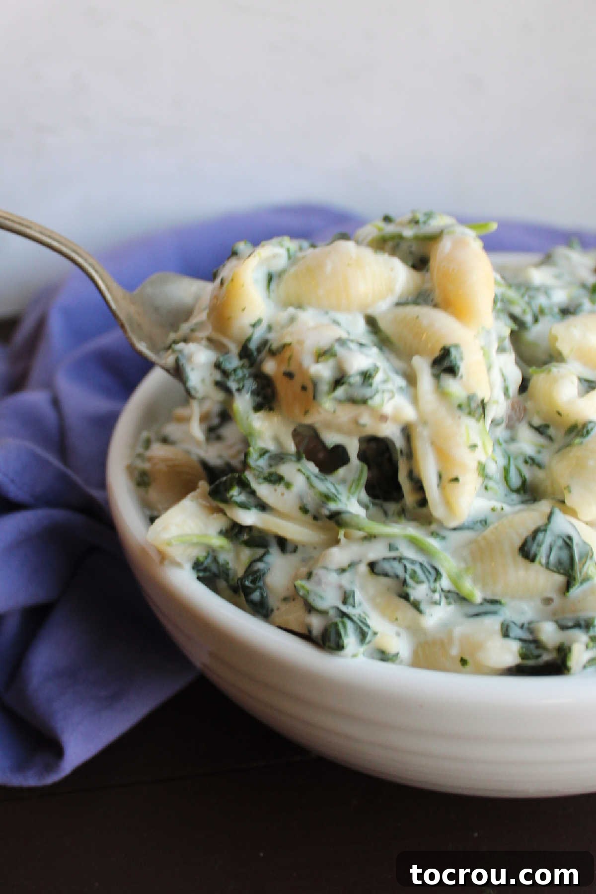 Velvety Spinach Macaroni Bake 5 A serving spoon gracefully scoops out a generous helping of cheesy white macaroni and cheese, rich with spinach, from a large pot.