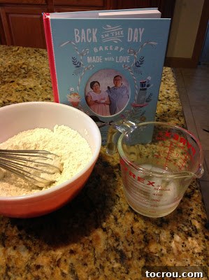 Pie Crust Ingredients Prepped Flour mixture in bowl with whisk, ice water in measuring cup and cook book, ready to make pie crust pastry.