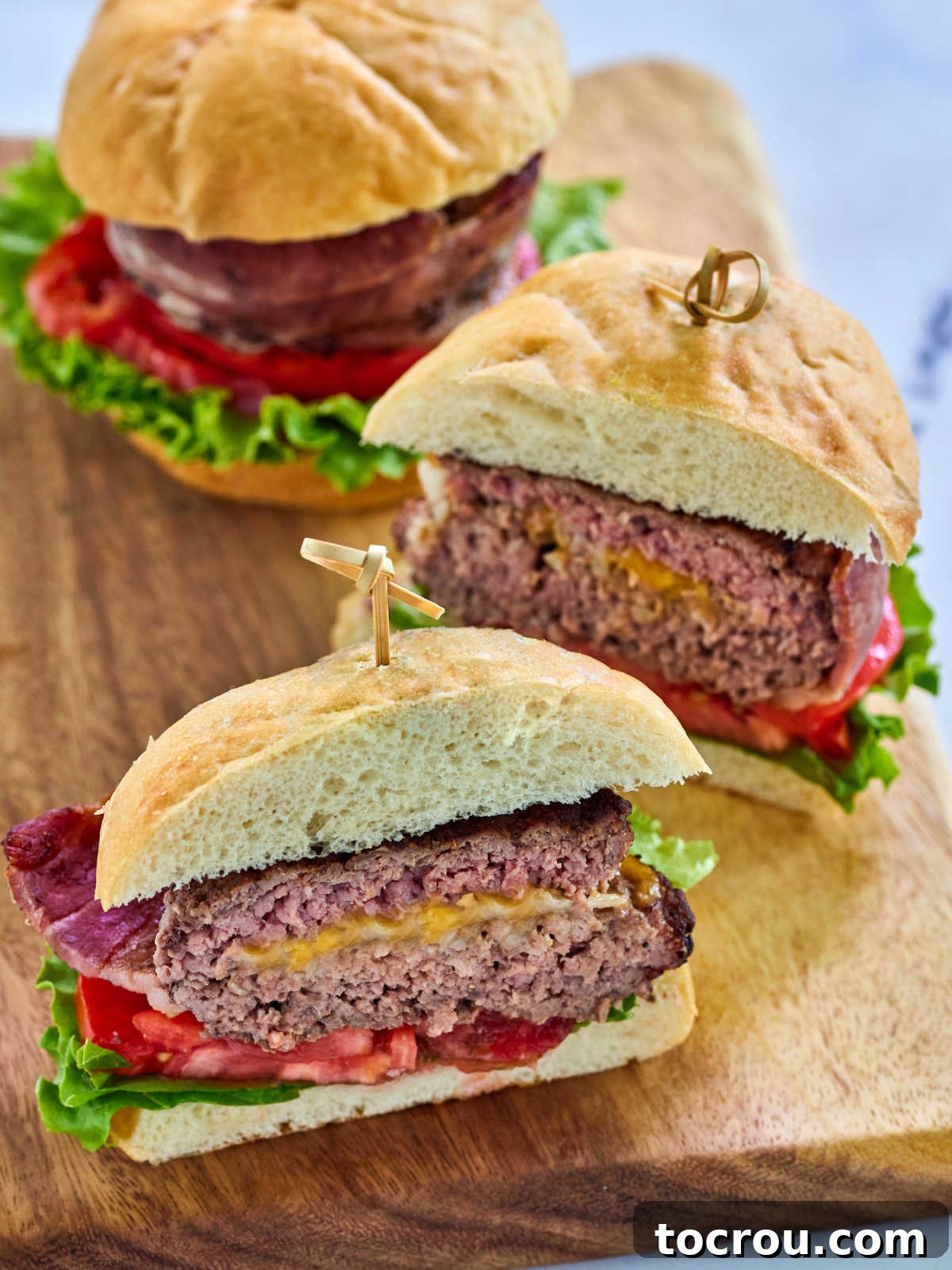 Maw-Maws Unexpected Burger Bliss 6 Cooked hamburger surprise on bun with tomato and lettuce showing melted cheese and onion interior and crispy bacon wrap. A truly appetizing display of a finished Maw-Maw's burger.