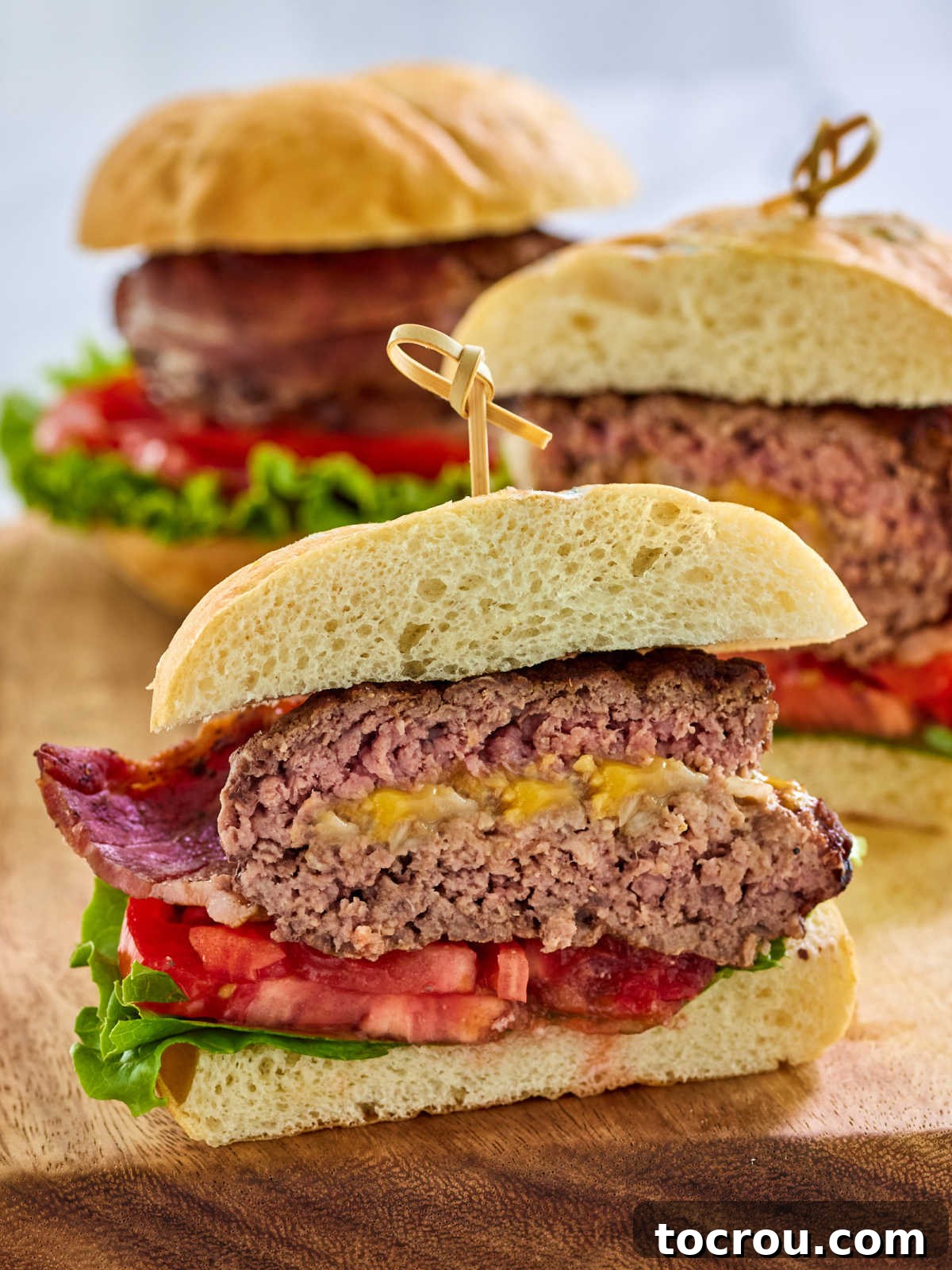 Maw-Maws Unexpected Burger Bliss 7 Half of a stuffed hamburger surprise with melted cheese and onion inside with bacon on the outside served on a bun with lettuce and tomato. A close-up view highlighting the delicious interior.