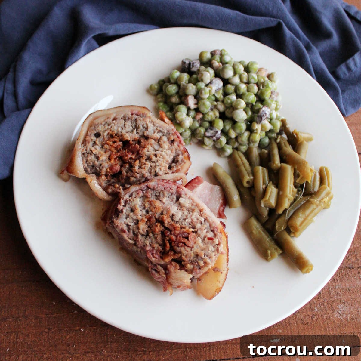 Dinner plate with two slices of bacon explosion, pea salad, and green beans.