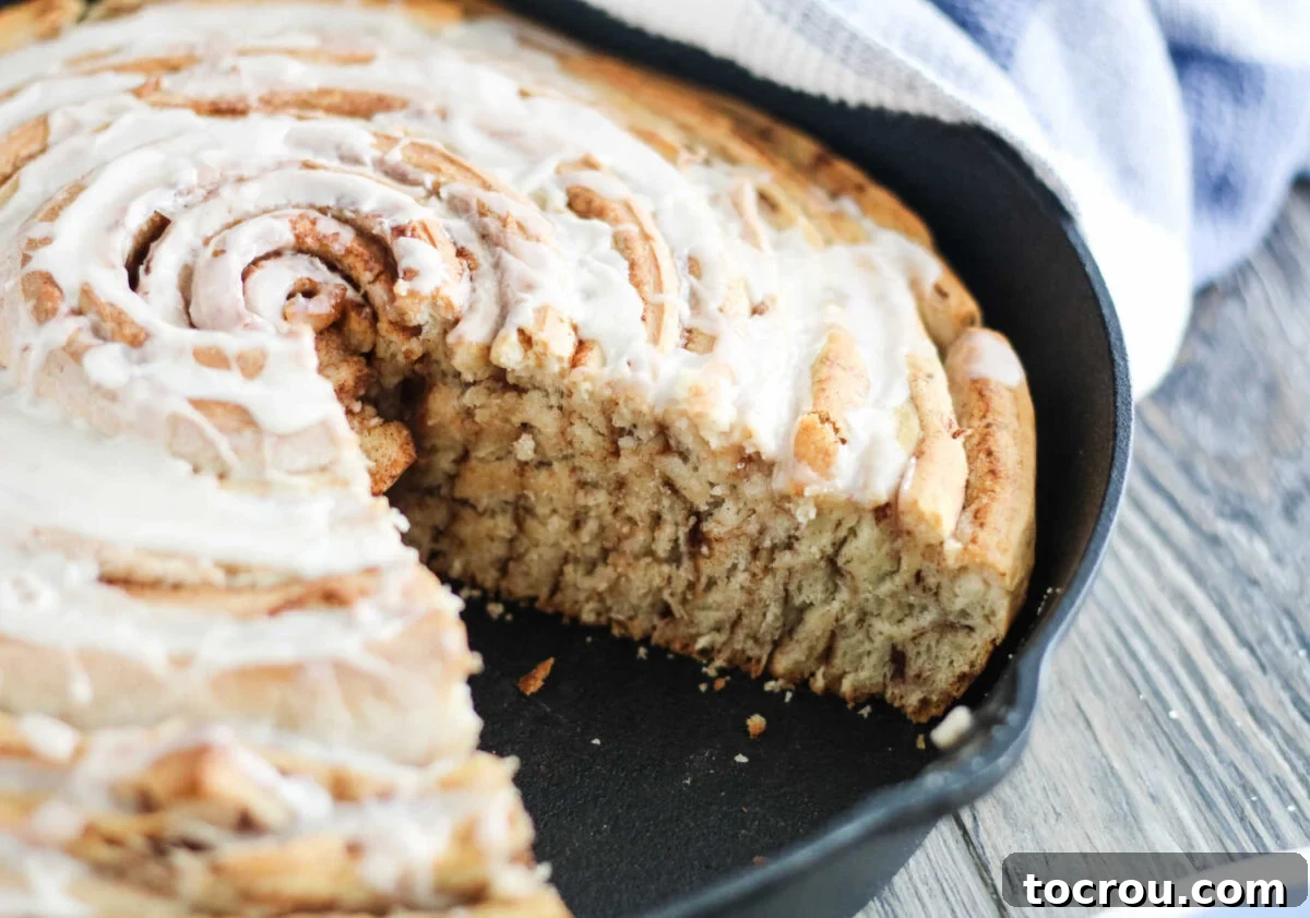 Large cinnamon roll cake in cast iron pan with a slice missing showing the layers cinnamon filling.