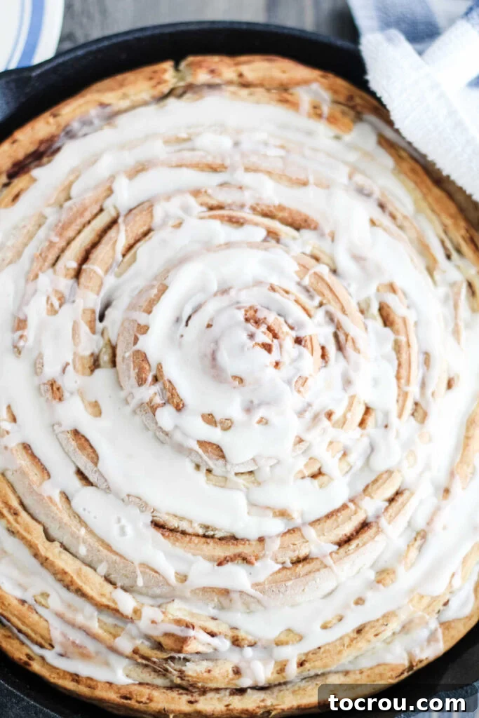 Close up of skillet full of large cinnamon roll with white glaze.