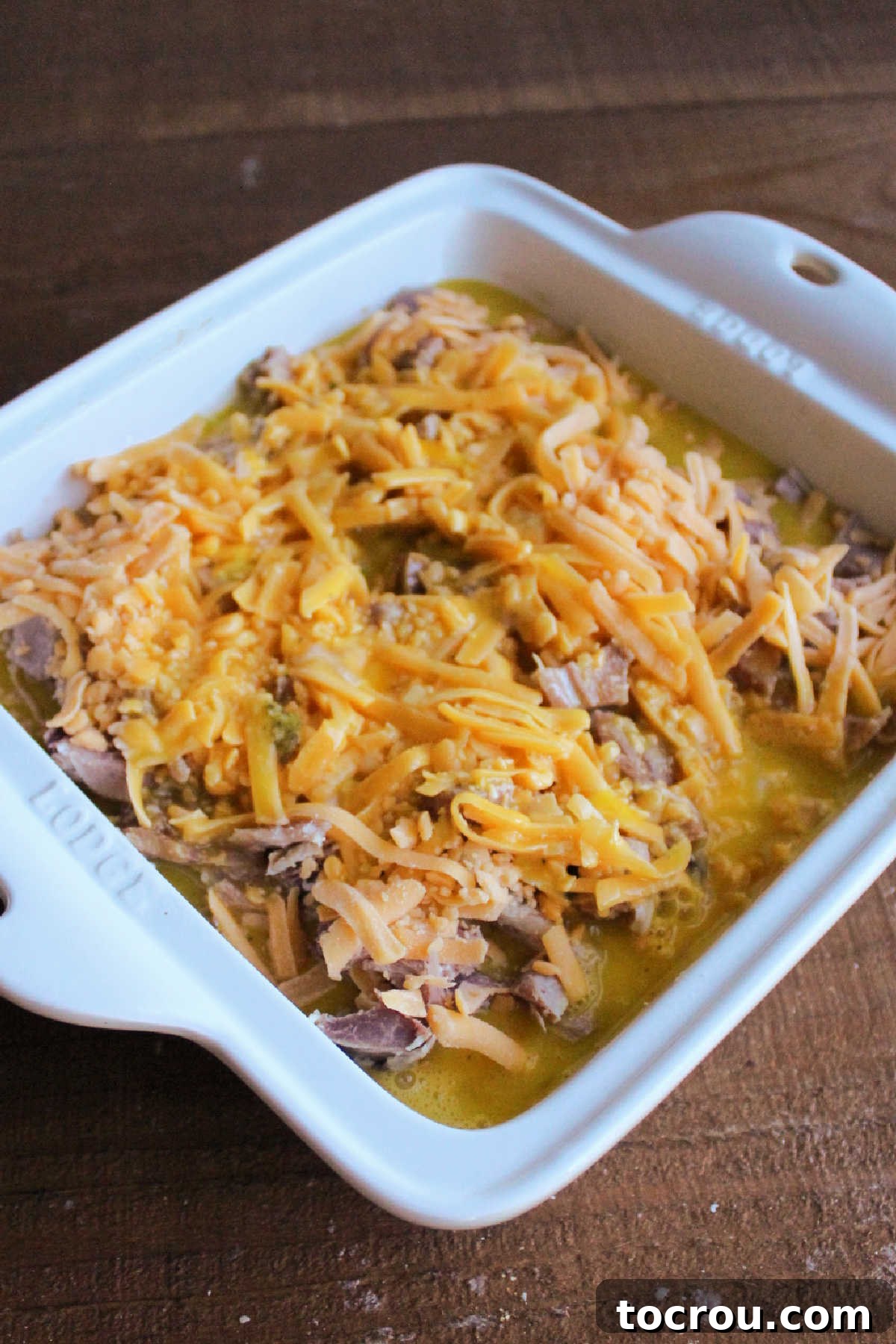 Casserole Prepped for Baking The assembled tater tot egg casserole, showcasing how the beaten eggs have been poured over the ham and cheese but haven't yet puffed up to completely cover everything before baking.