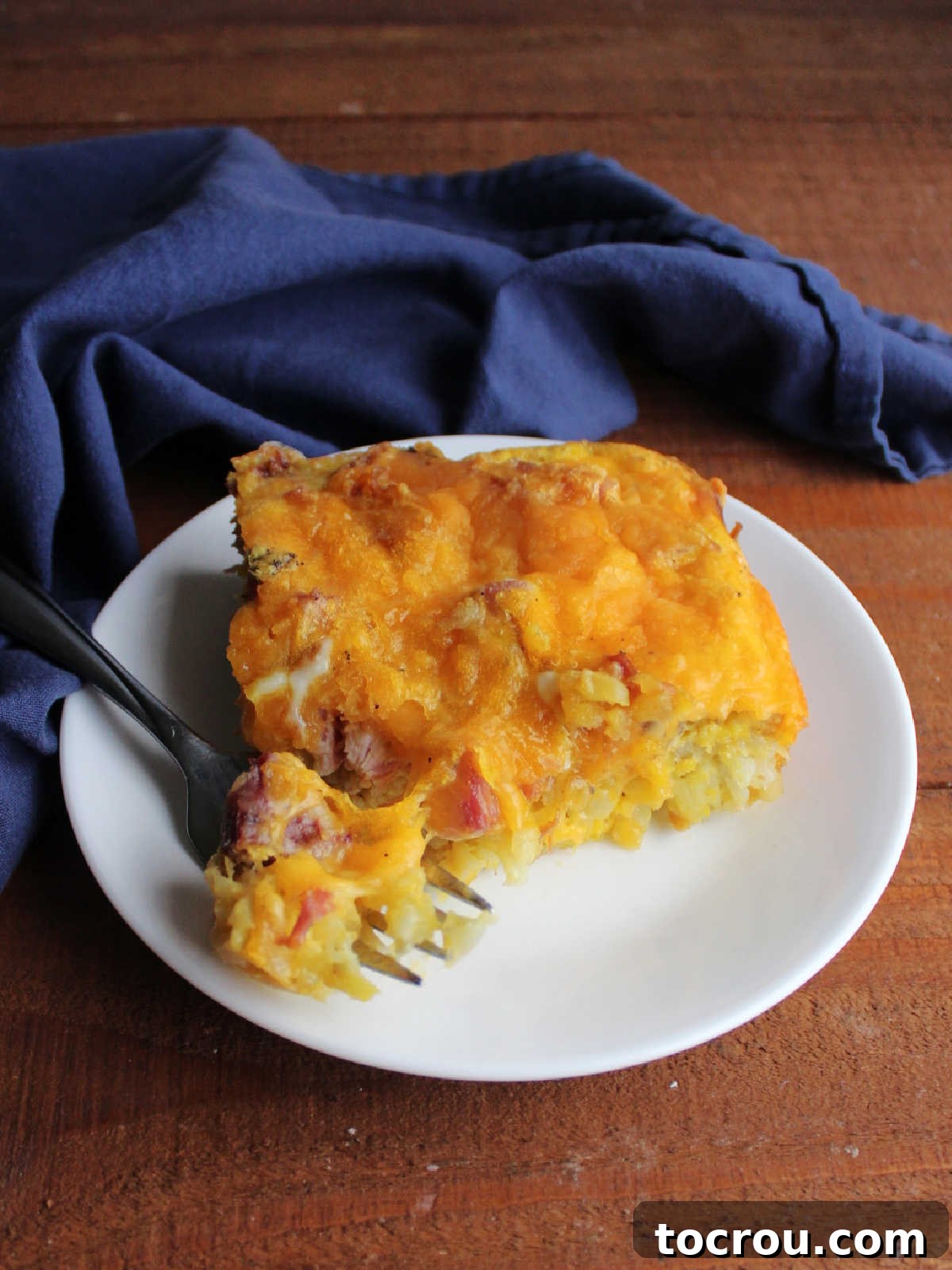 Perfect Bite of Casserole A fork holding a perfect bite of the casserole, clearly showing scrambled eggs, melted cheese, a piece of ham, and a tater tot baked together.