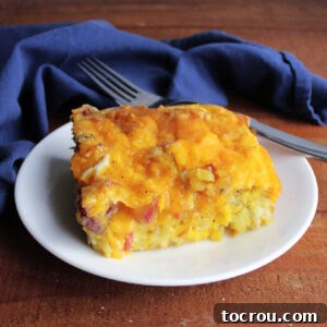 A mouth-watering piece of egg and ham tater tot breakfast casserole on a plate, perfectly baked and ready to eat.