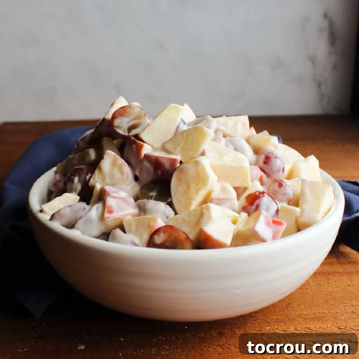 Delicious Grape Apple Salad with Yogurt Dressing White serving bowl piled high with grape and apple salad dressed with a cinnamon and honey yogurt dressing.