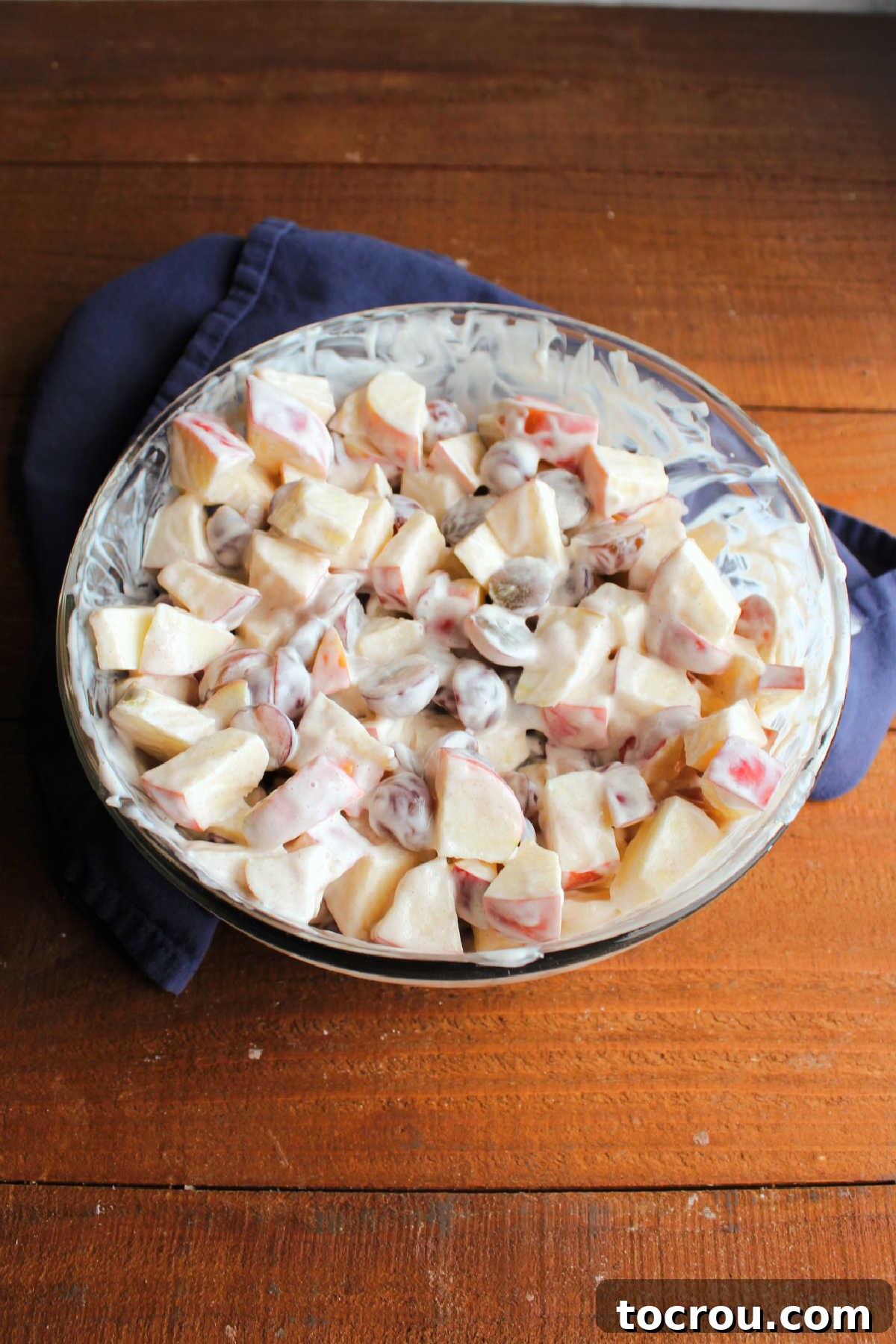 Mixing apples and grapes with yogurt dressing. Large mixing bowl filled with chunks of apple and grape halves coated in cinnamon, honey, yogurt dressing.