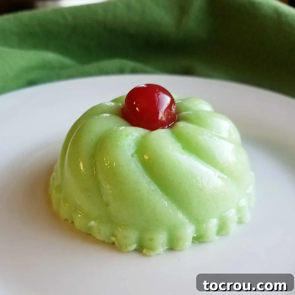 small green molded jello salad with maraschino cherry on top.